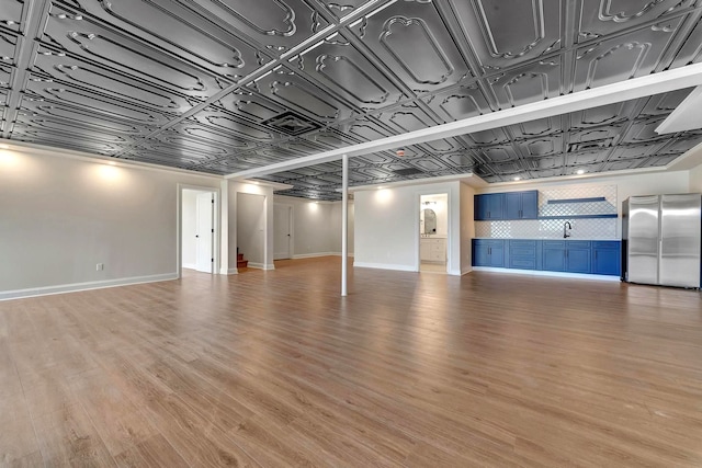 basement featuring light wood-type flooring, stainless steel refrigerator, and sink