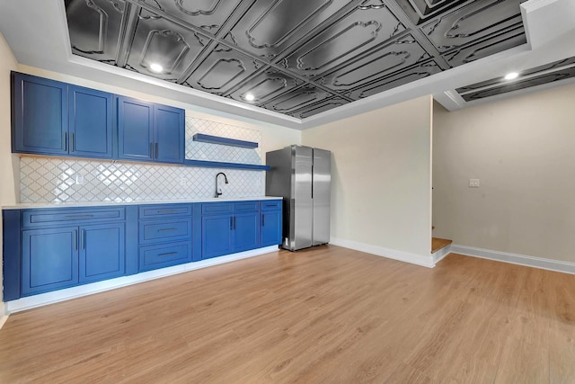 kitchen featuring backsplash, blue cabinets, sink, light hardwood / wood-style floors, and stainless steel refrigerator