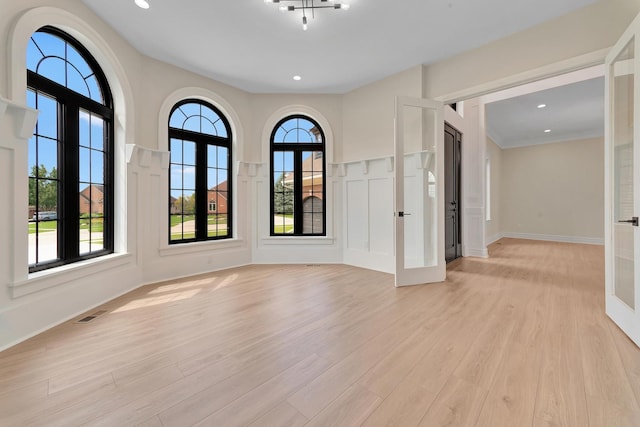 empty room with light hardwood / wood-style floors, crown molding, and french doors