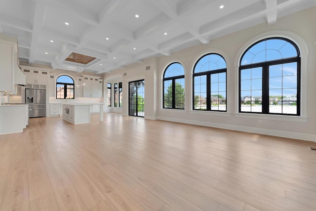 unfurnished living room with beam ceiling, plenty of natural light, and light hardwood / wood-style floors