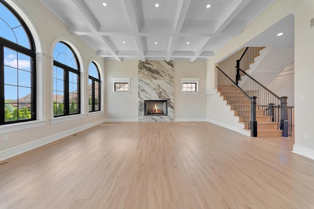 unfurnished living room featuring beamed ceiling, light hardwood / wood-style floors, a healthy amount of sunlight, and a premium fireplace