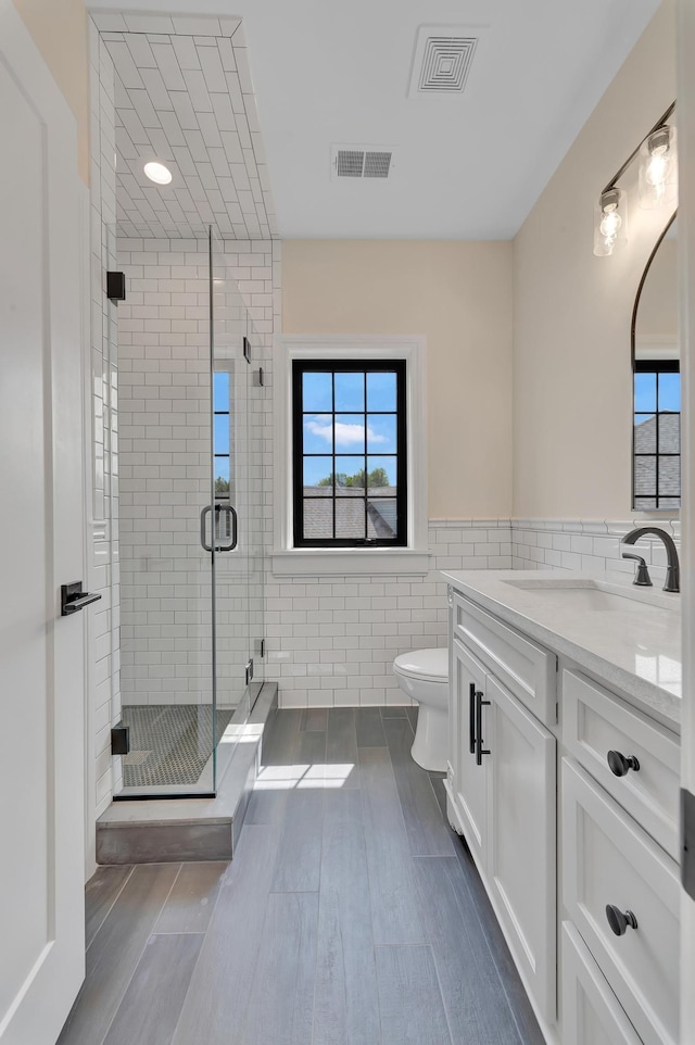 bathroom featuring walk in shower, vanity, wood-type flooring, tile walls, and toilet