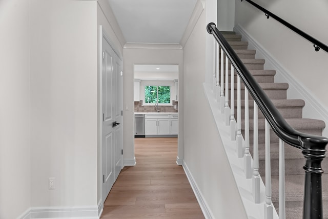 stairway featuring wood-type flooring, crown molding, and sink