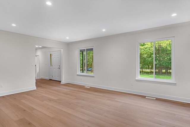 empty room with light hardwood / wood-style floors, a wealth of natural light, and crown molding