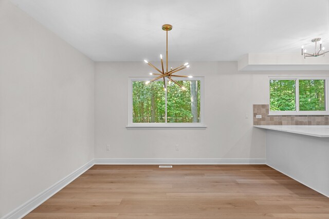 unfurnished dining area with light hardwood / wood-style floors, an inviting chandelier, and a healthy amount of sunlight