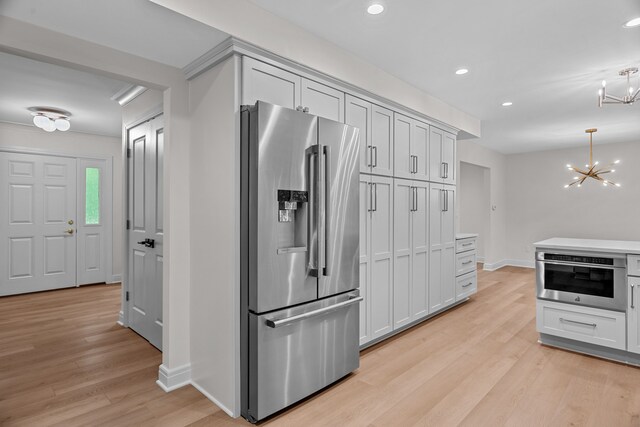 kitchen with appliances with stainless steel finishes, decorative light fixtures, light hardwood / wood-style floors, white cabinetry, and a chandelier