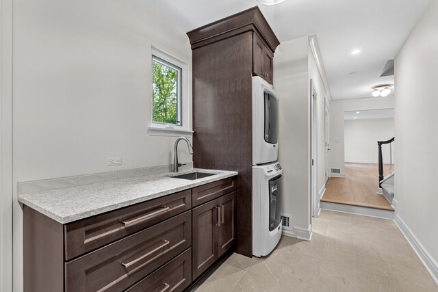 kitchen featuring dark brown cabinetry, sink, and stacked washing maching and dryer