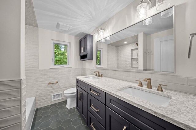 bathroom featuring tile patterned floors, walk in shower, vanity, tile walls, and toilet