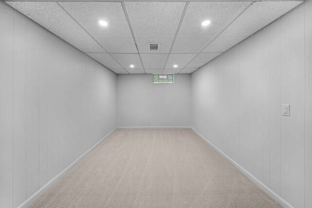 unfurnished room with a drop ceiling, wood walls, and light carpet