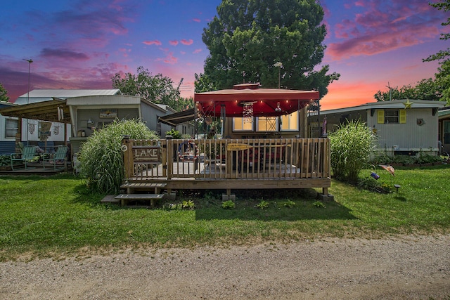 back house at dusk with a wooden deck and a yard