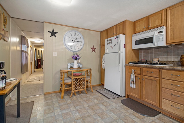 kitchen with backsplash, white appliances, a textured ceiling, wooden walls, and dark stone countertops