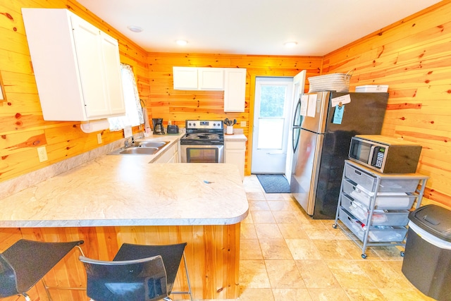 kitchen featuring sink, stainless steel appliances, kitchen peninsula, wood walls, and white cabinets