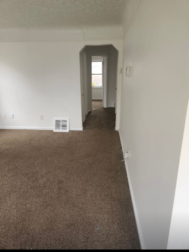 spare room featuring a textured ceiling and dark carpet