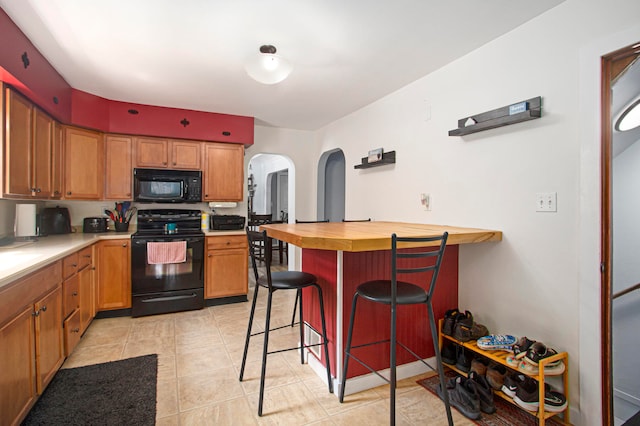 kitchen featuring black appliances, butcher block countertops, a kitchen bar, and light tile patterned floors