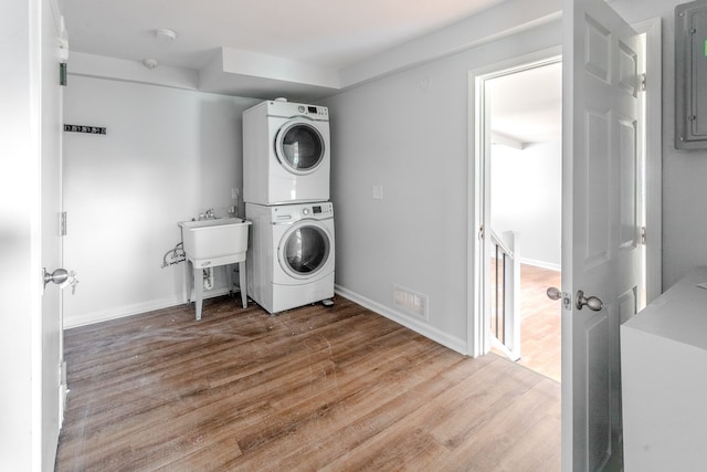 laundry area with sink, stacked washer / drying machine, and light hardwood / wood-style flooring