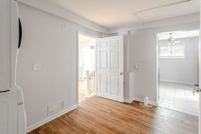 unfurnished room with stacked washer and clothes dryer, ceiling fan, and light wood-type flooring