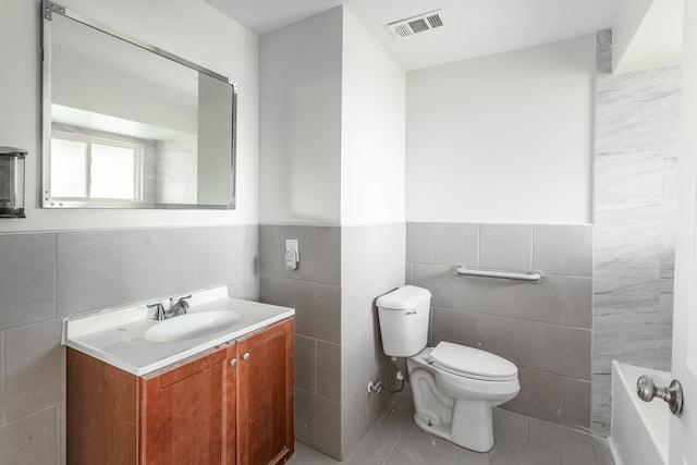 bathroom featuring tile patterned flooring, tile walls, toilet, a tub, and vanity