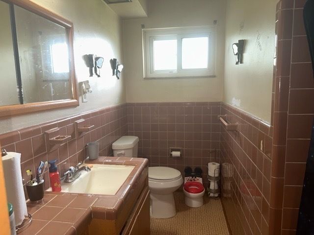 bathroom with tile patterned flooring, vanity, toilet, and tile walls