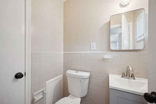 half bathroom with toilet, a wainscoted wall, vanity, and tile walls