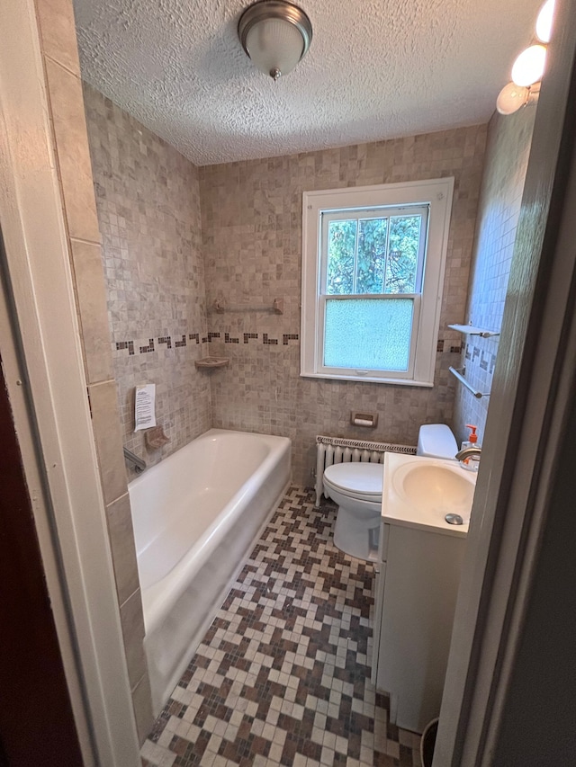 bathroom featuring a tub, radiator, a textured ceiling, vanity, and tile walls