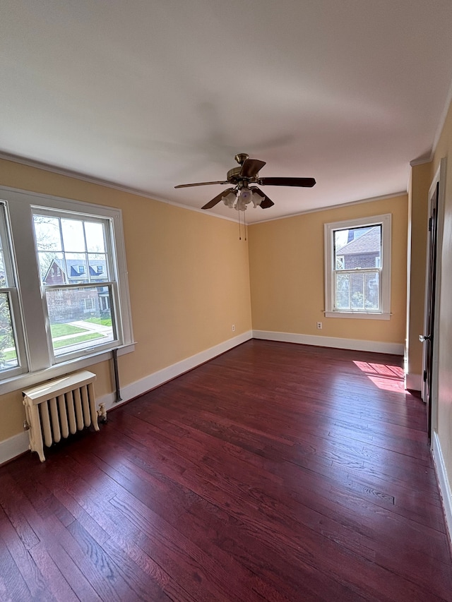 empty room with a wealth of natural light, ceiling fan, dark wood-type flooring, and radiator