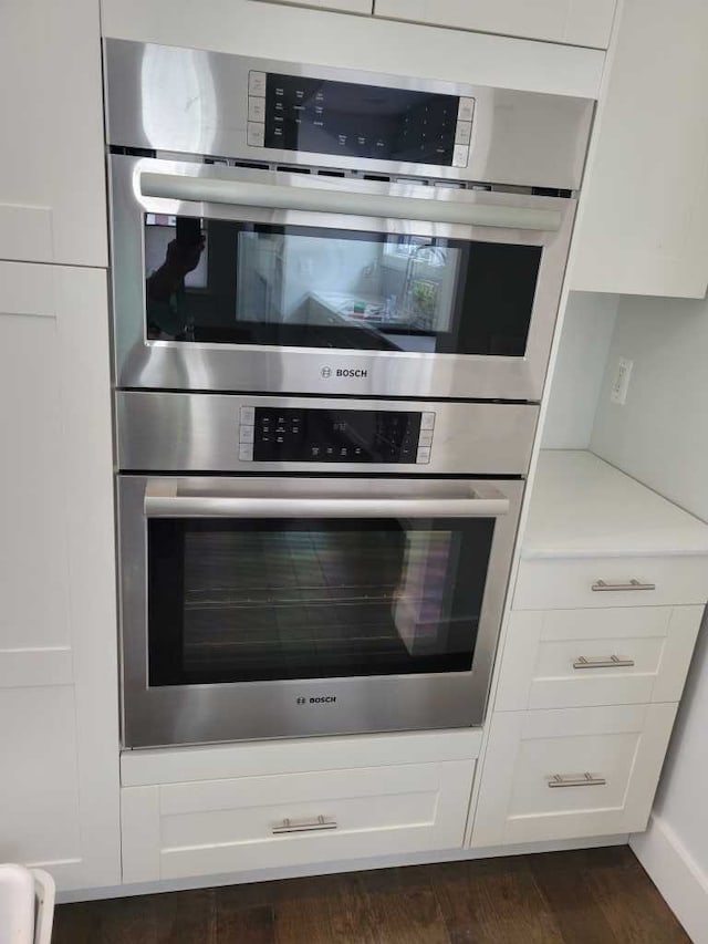 kitchen with double oven, white cabinetry, and dark hardwood / wood-style floors