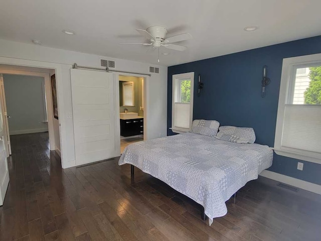 bedroom featuring a barn door, ensuite bath, ceiling fan, and dark wood-type flooring