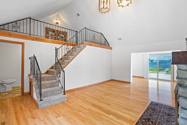 1794 S Hughes Rd, Brighton, MI 48114 - unfurnished living room featuring high vaulted ceiling, wood finished floors, stairway, and a chandelier