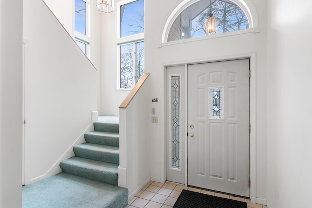 foyer entrance with a towering ceiling, light tile patterned floors, and a notable chandelier