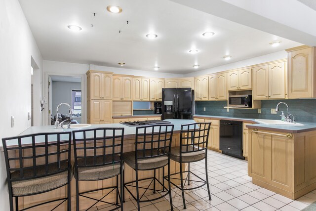 kitchen with light brown cabinetry, sink, an island with sink, and black appliances