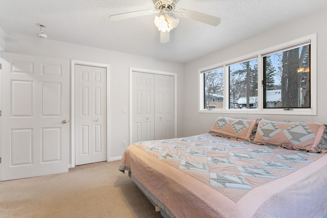 carpeted bedroom with ceiling fan, a textured ceiling, and multiple closets