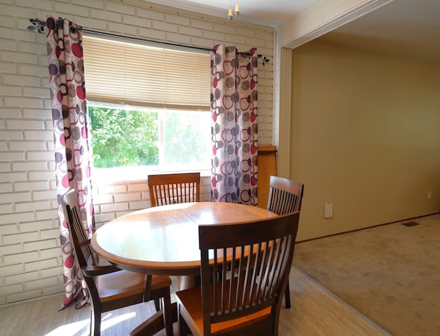 dining area featuring light colored carpet and brick wall