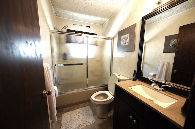 full bathroom with tile patterned floors, bath / shower combo with glass door, vanity, a textured ceiling, and tile walls