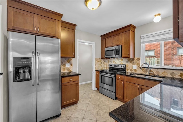 kitchen with light tile patterned floors, stainless steel appliances, dark stone countertops, and sink