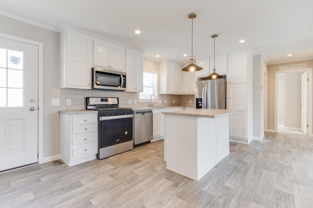 kitchen with a center island, light wood-type flooring, appliances with stainless steel finishes, decorative light fixtures, and white cabinetry