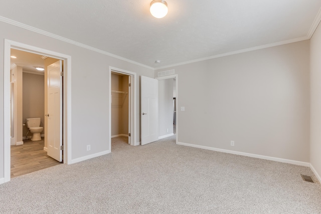 unfurnished bedroom featuring a closet, crown molding, ensuite bathroom, and light colored carpet