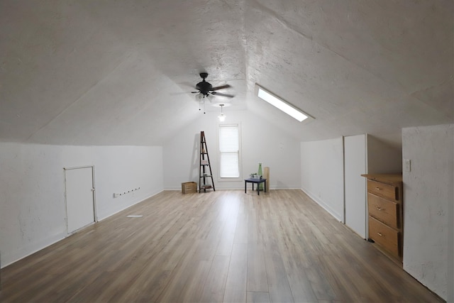 additional living space featuring hardwood / wood-style flooring, ceiling fan, and vaulted ceiling with skylight