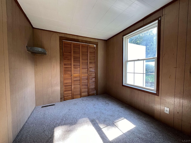 unfurnished bedroom with carpet flooring, wooden walls, and a closet