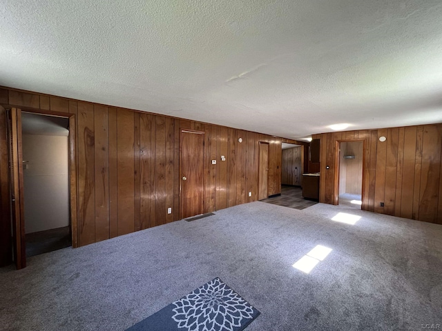 unfurnished living room with a textured ceiling, dark carpet, and wood walls