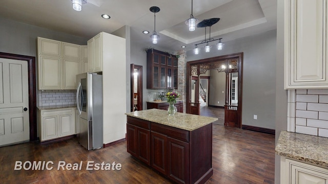 kitchen featuring pendant lighting, dark wood-type flooring, a raised ceiling, stainless steel fridge, and light stone counters