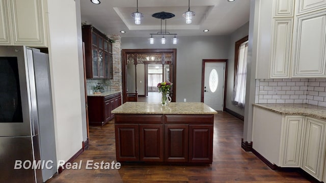 kitchen with dark wood-type flooring, a raised ceiling, hanging light fixtures, decorative backsplash, and stainless steel fridge