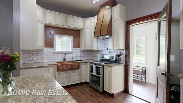 kitchen with light stone countertops, range with two ovens, a wealth of natural light, and custom exhaust hood