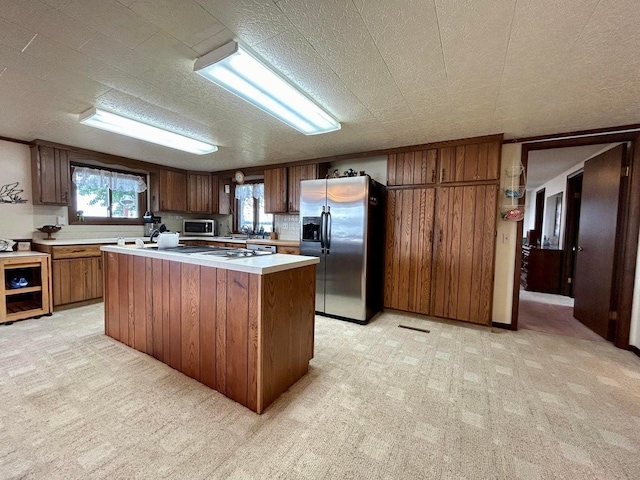 kitchen featuring a textured ceiling, a center island, stainless steel appliances, and light carpet