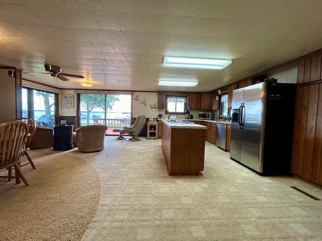 kitchen featuring wood walls, light carpet, ceiling fan, a textured ceiling, and appliances with stainless steel finishes