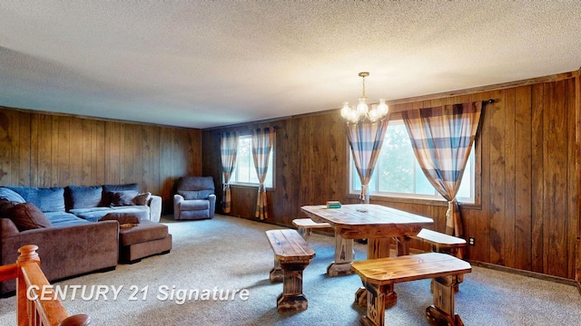 carpeted dining room featuring wood walls, a textured ceiling, and an inviting chandelier