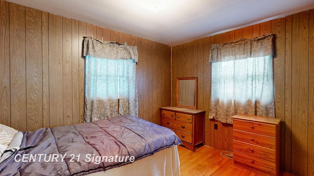 bedroom with light wood-type flooring and wood walls