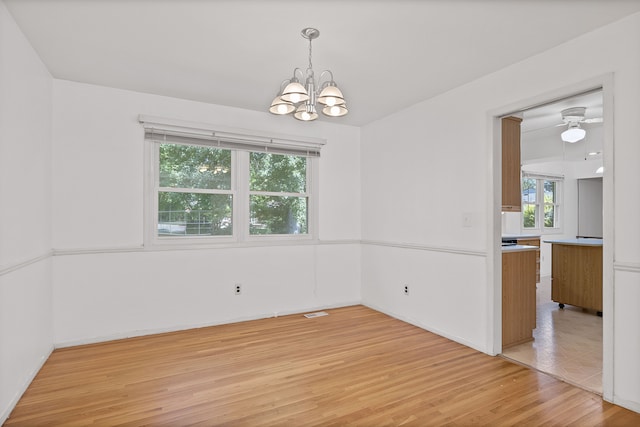 unfurnished dining area featuring ceiling fan with notable chandelier and light hardwood / wood-style floors