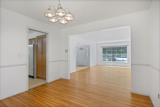 empty room with an inviting chandelier and light hardwood / wood-style flooring