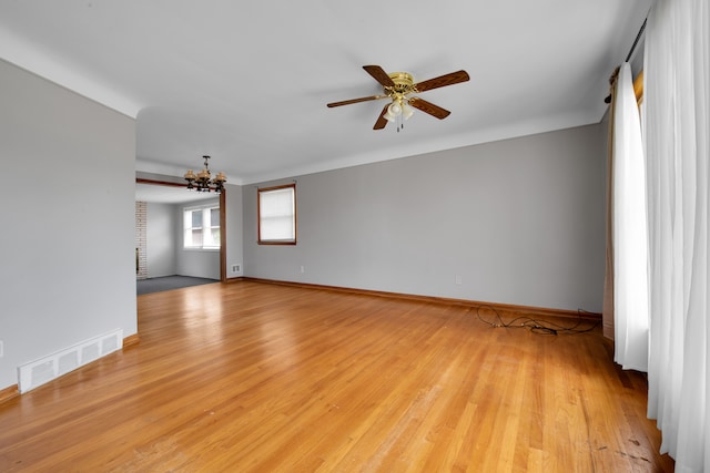 empty room featuring ceiling fan with notable chandelier and light hardwood / wood-style flooring