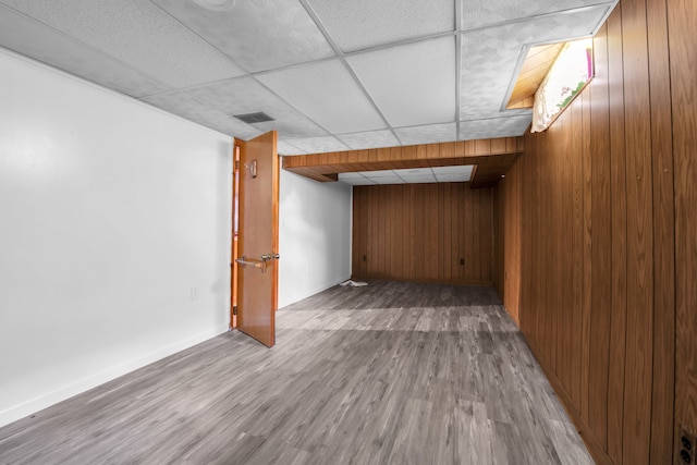 basement featuring a paneled ceiling, wooden walls, and light wood-type flooring